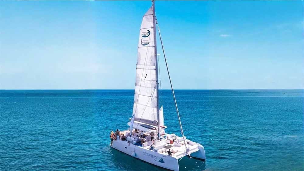 Un catamarán blanco navegando sobre un océano azul en calma bajo un cielo despejado.