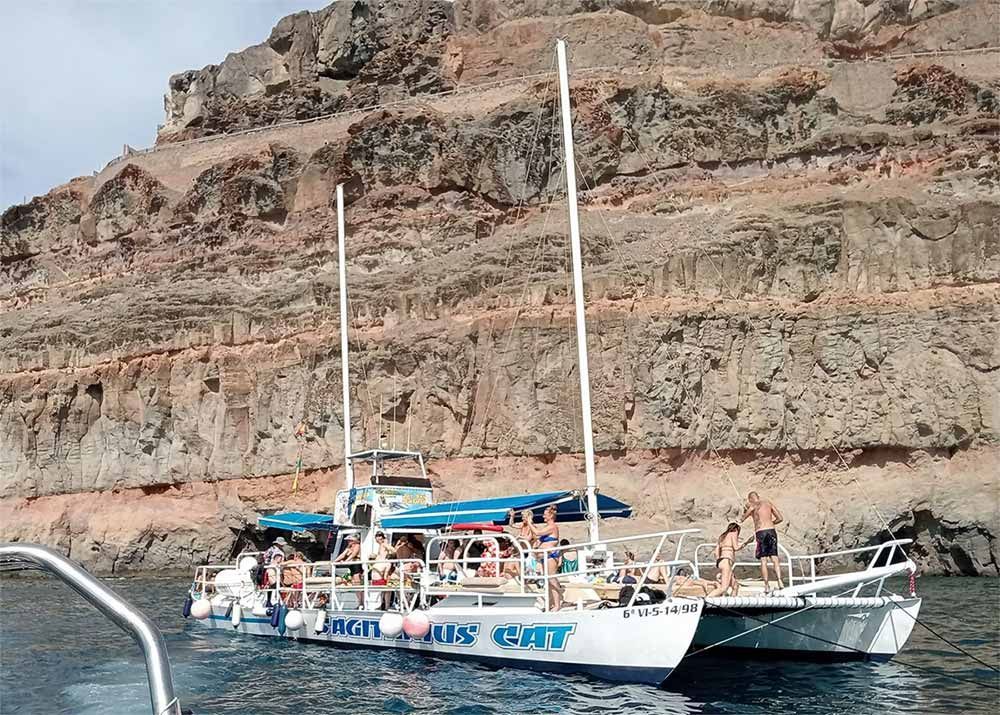 Velero con pasajeros en aguas tranquilas junto a un acantilado rocoso.