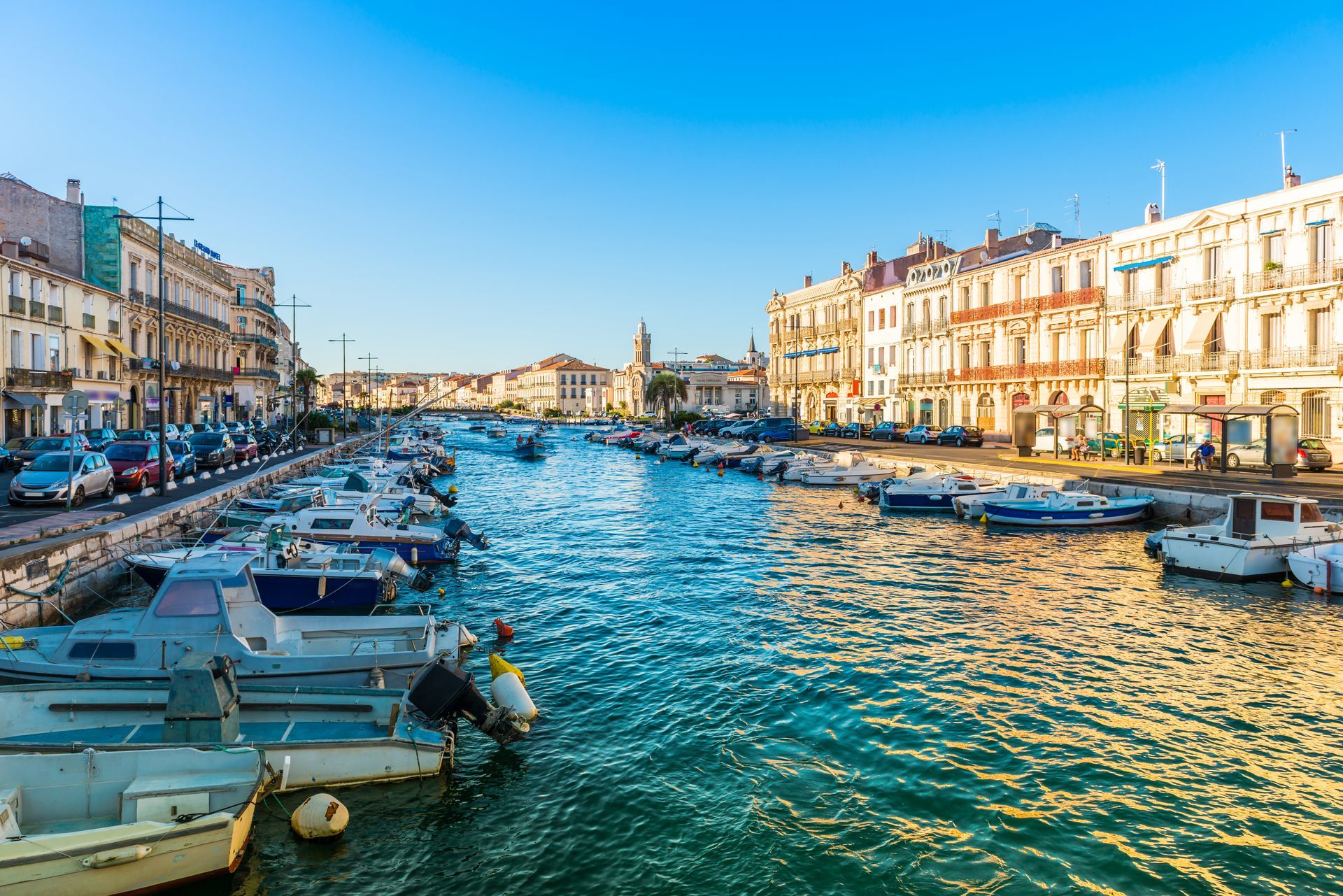 Canal ensoleillé du port avec des bateaux et des bâtiments riverains sous un ciel bleu.