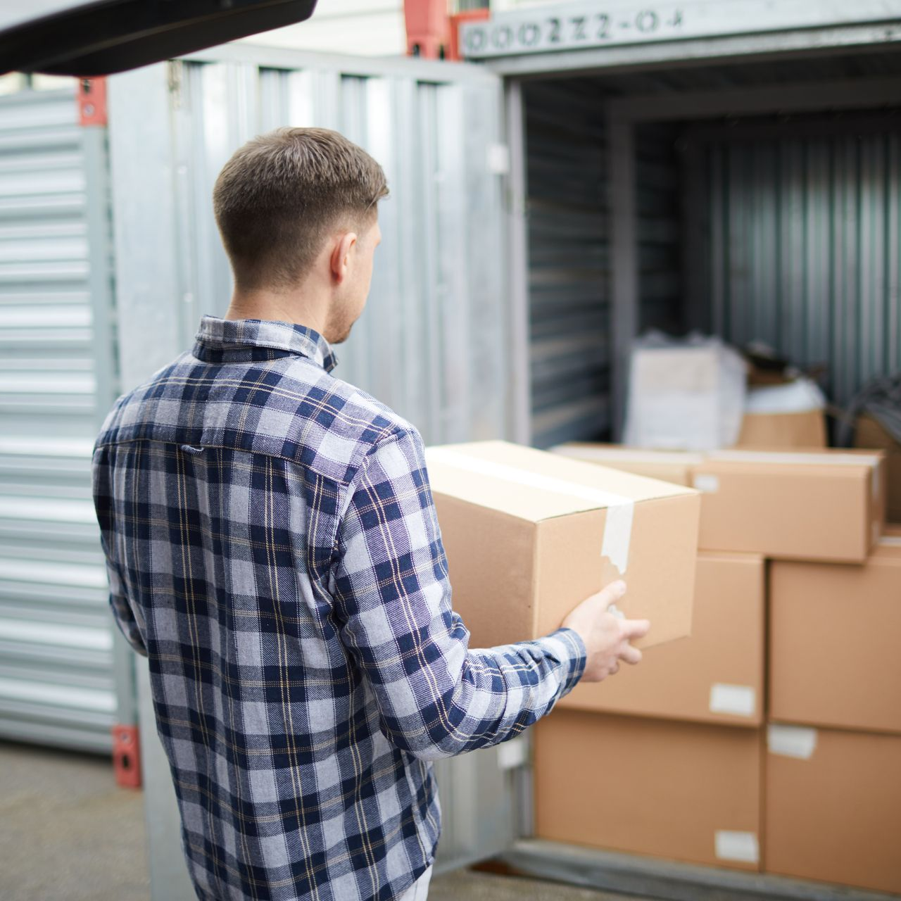 Une personne transporte un carton dans un conteneur de stockage parmi des cartons empilés.
