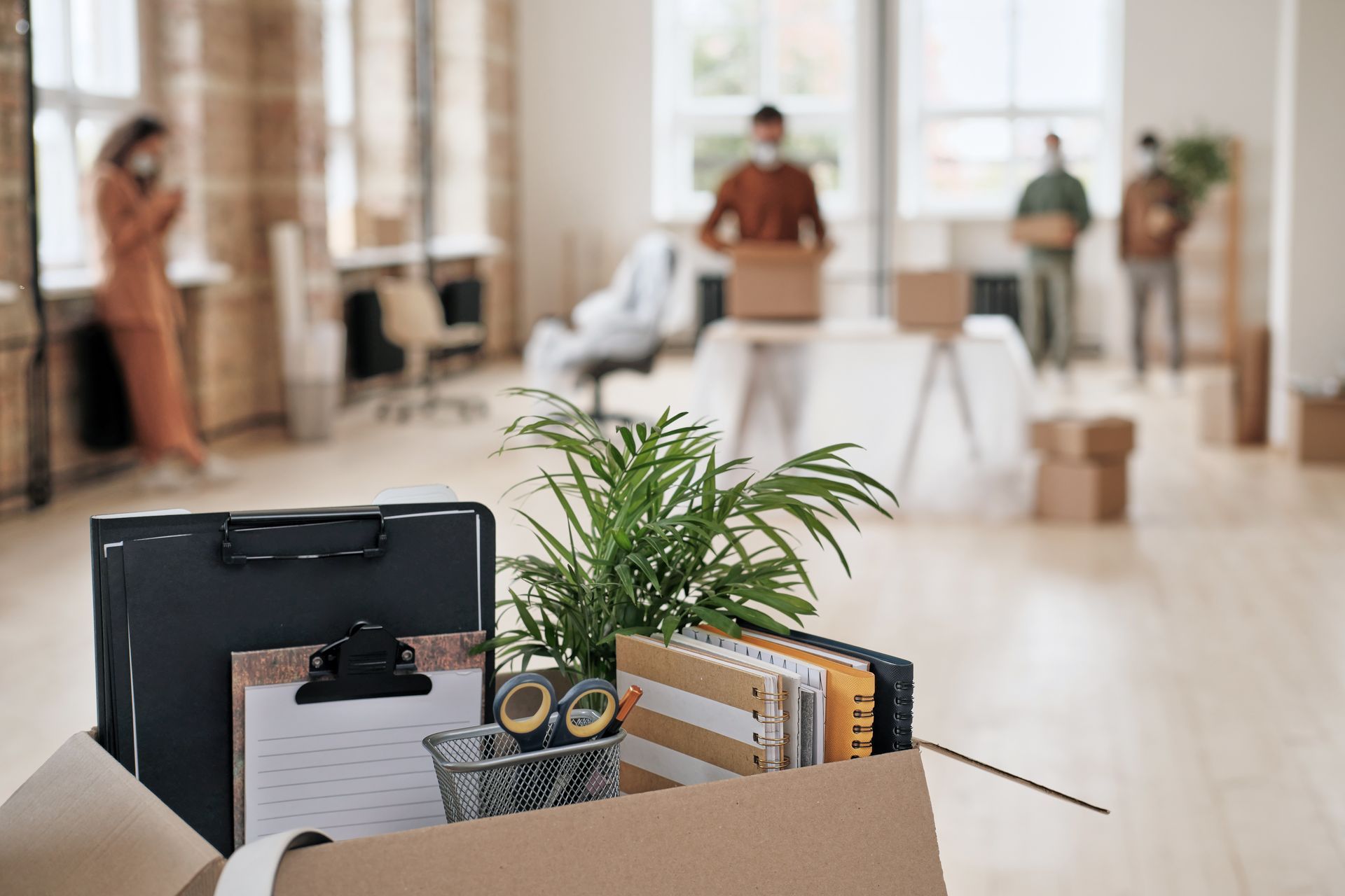 Hall d'entrée d'un immeuble de bureaux avec un carton de déménagement au premier plan, un bloc-notes, une plante et des personnes floues en arrière-plan.