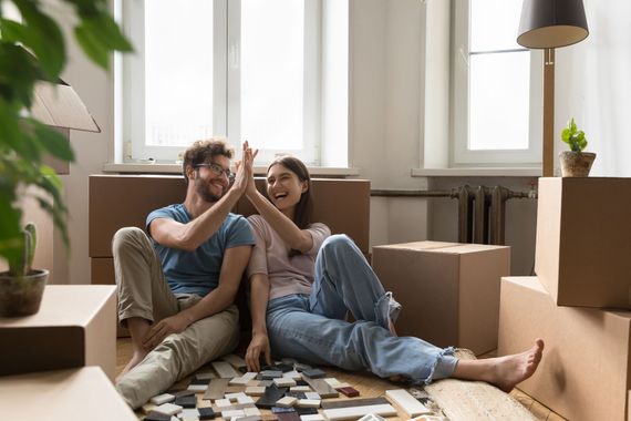 Un couple se tape dans la main dans une pièce ensoleillée, entouré de cartons de déménagement et d'affaires emballées.