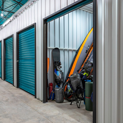 Une rangée de portes de box de stockage, dont une ouverte révèle des planches de surf, des vélos et divers équipements à l'intérieur.