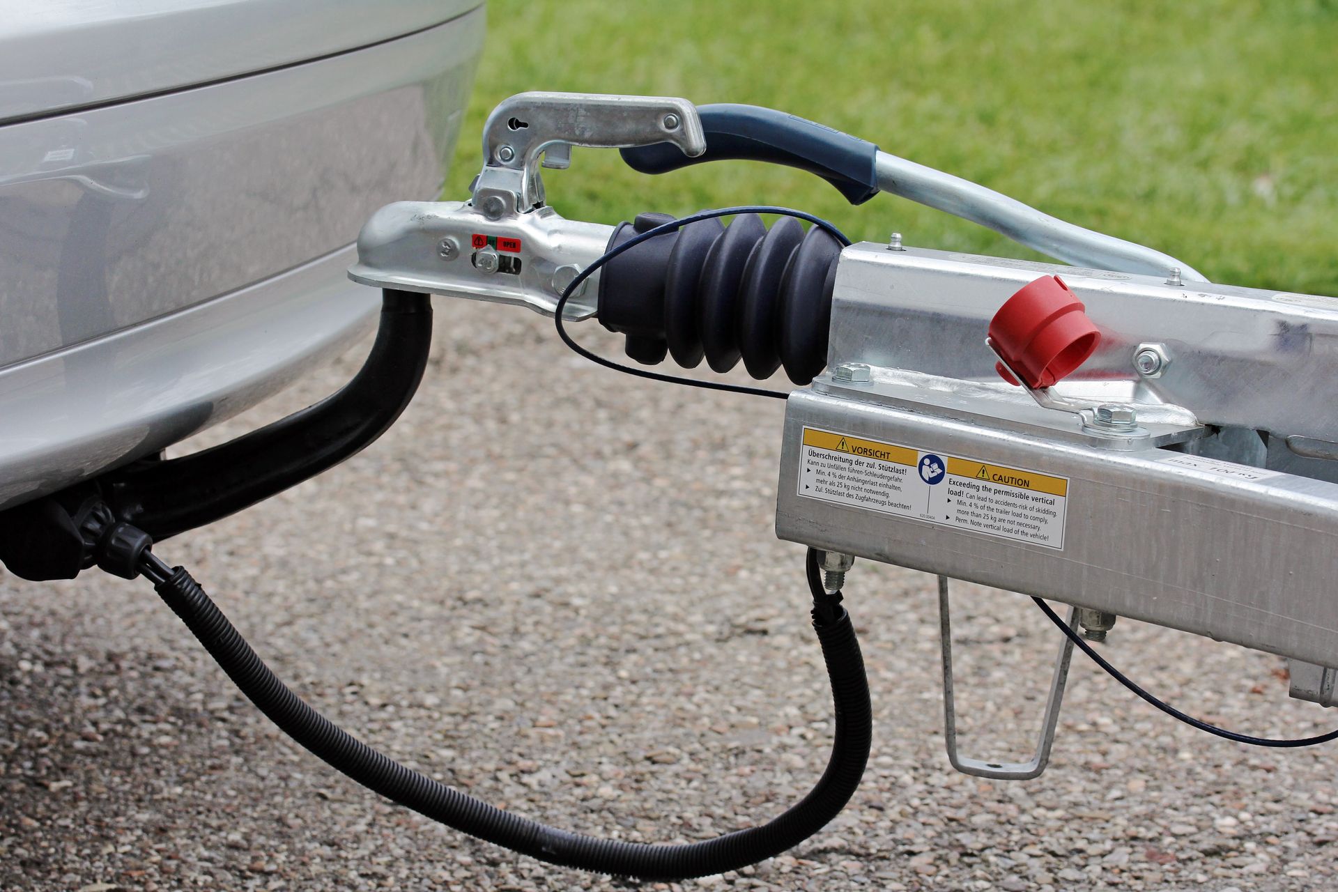 Attelage de remorque pour voiture relié à un véhicule argenté, avec chaînes de sécurité et un loquet de coupleur rouge.