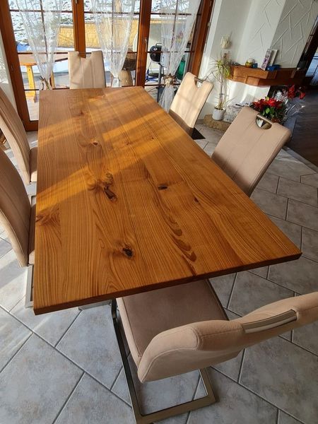 Ein Esstisch aus Holz mit sechs gepolsterten Stühlen in einem sonnendurchfluteten Raum.