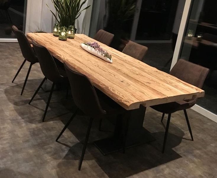 Holzesstisch mit acht dunklen Stühlen, Kerzen und Pflanzen.