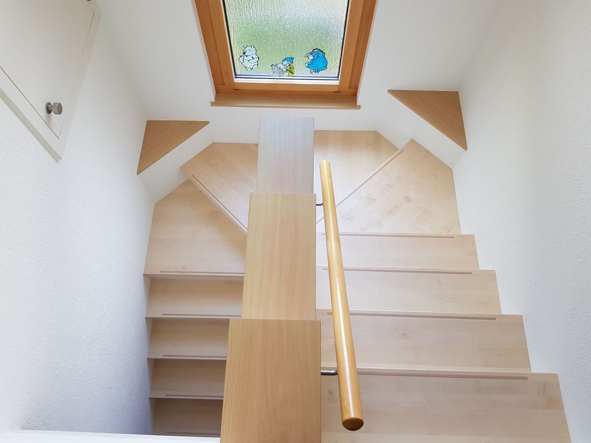 Treppe mit hellen Holzstufen, Oberlicht oben und Handlauf auf der rechten Seite.