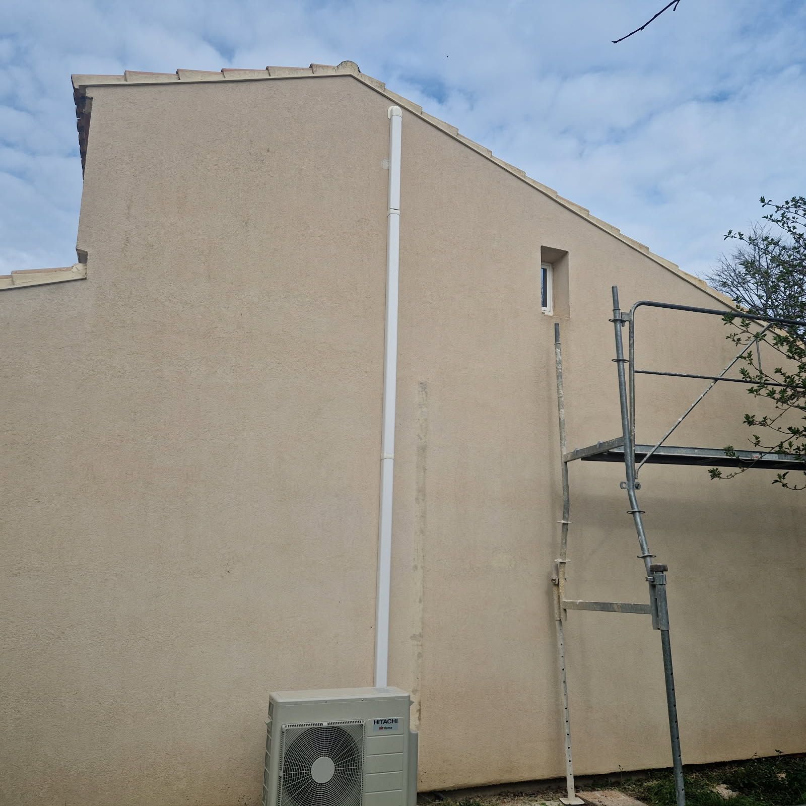 Bâtiment en stuc beige avec un tuyau blanc, une fenêtre, un échafaudage.