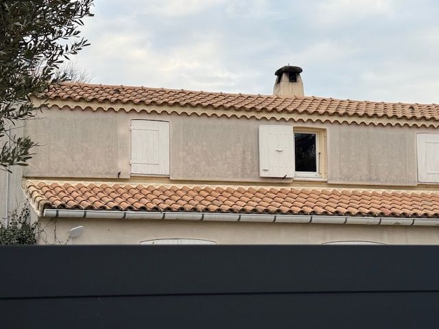 Un bâtiment de deux étages avec un toit de tuiles en terre cuite et des volets blancs ; une cheminée est visible sur le toit.