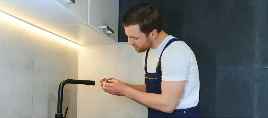 Un homme répare un évier dans une cuisine.
