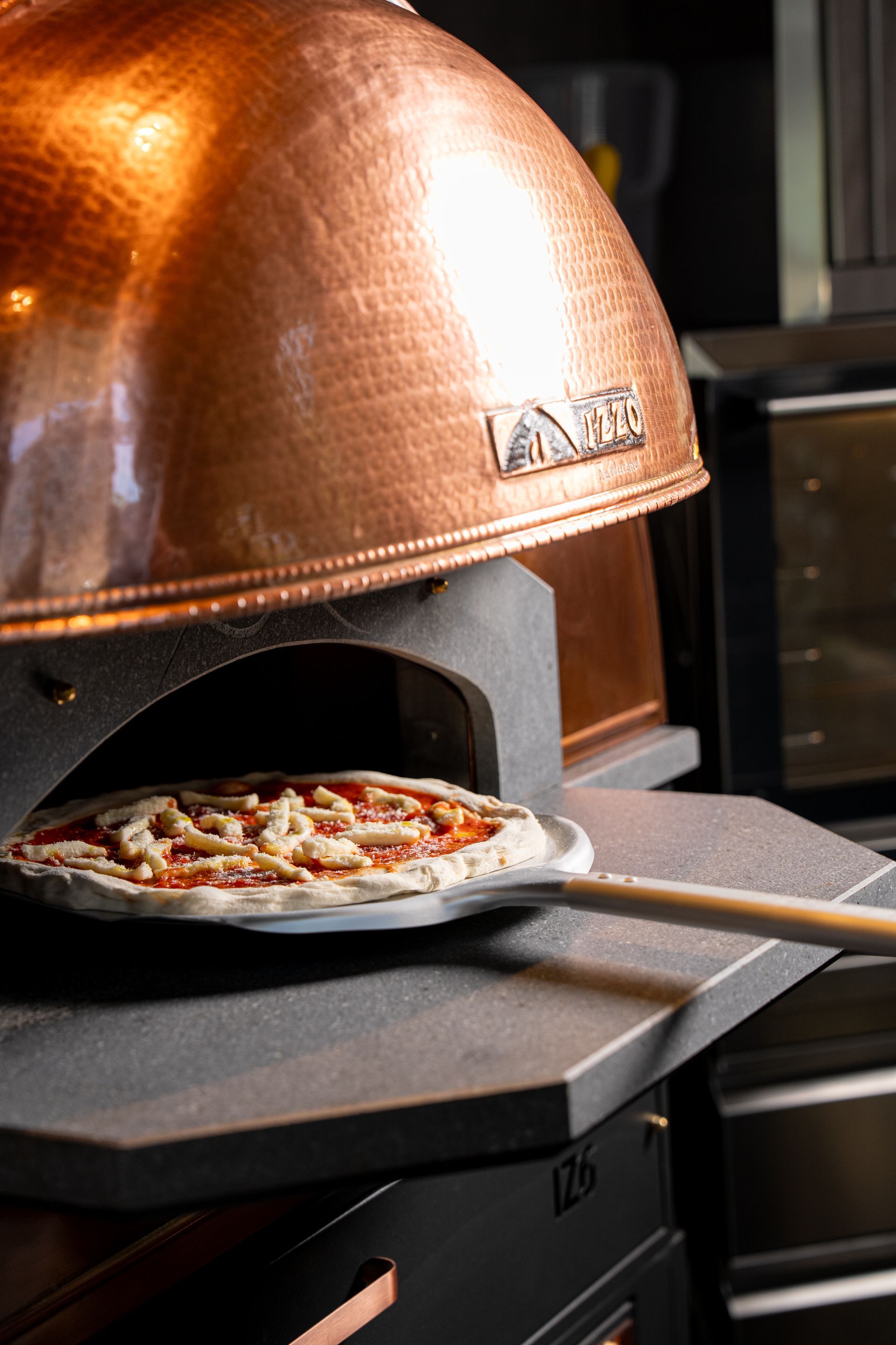 Pizza backt im Holzofen, Flammen lodern über dem Boden.