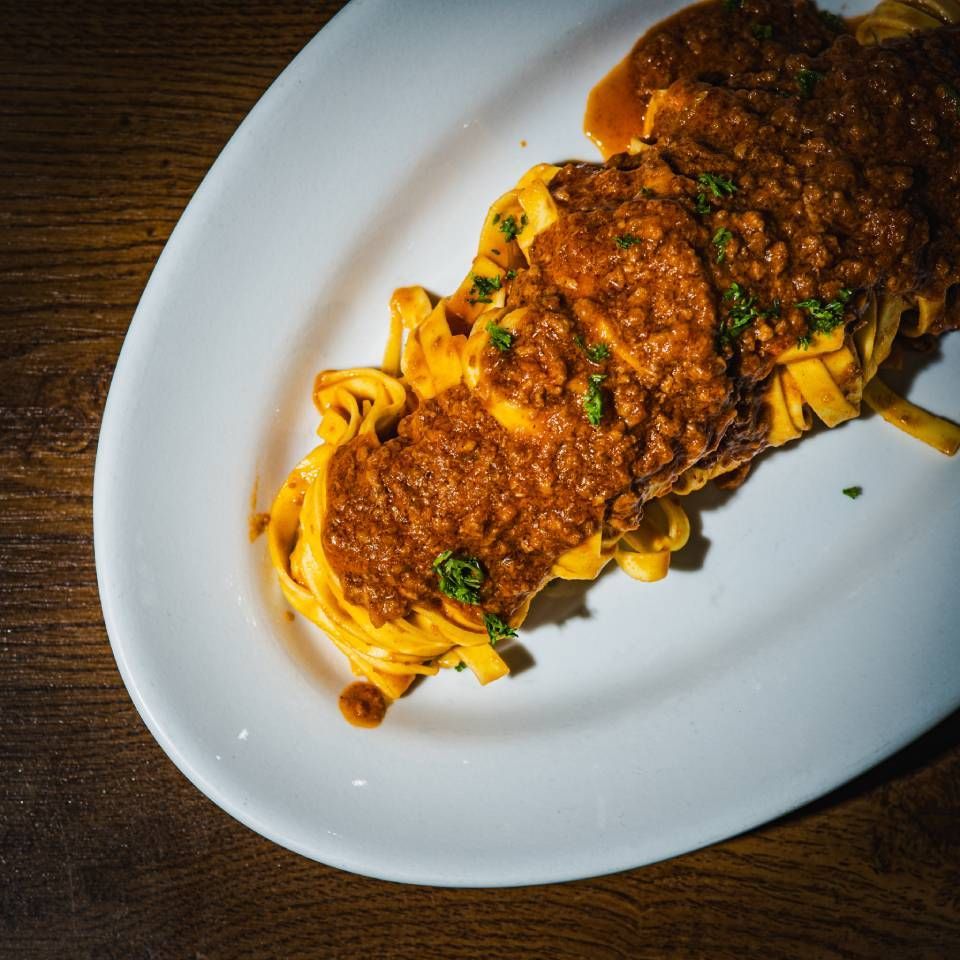 Tagliatelle-Nudeln mit reichhaltiger Fleischsosse auf einem weissen Teller, Holztisch.