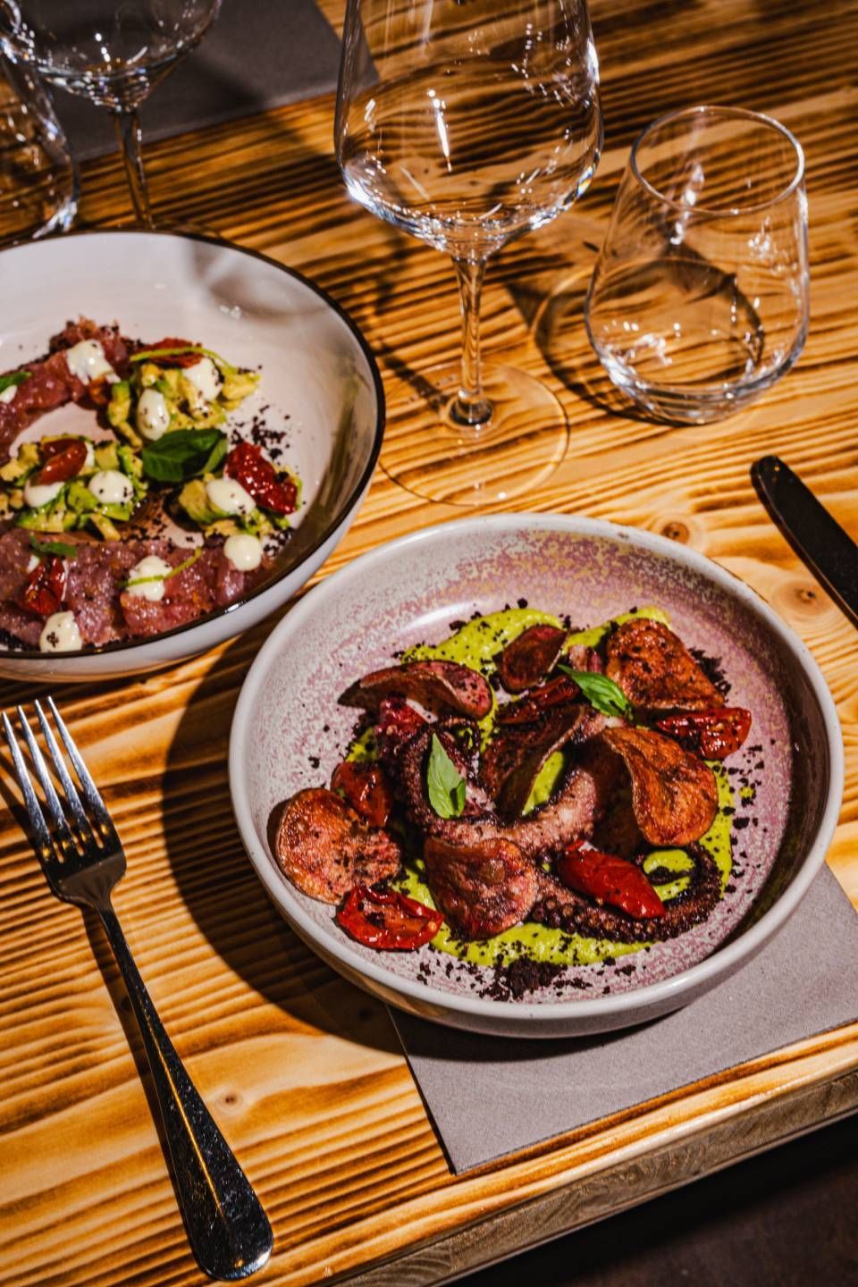 Zwei Teller mit Essen auf einem Holztisch, einer mit Oktopus, der andere mit Salat.