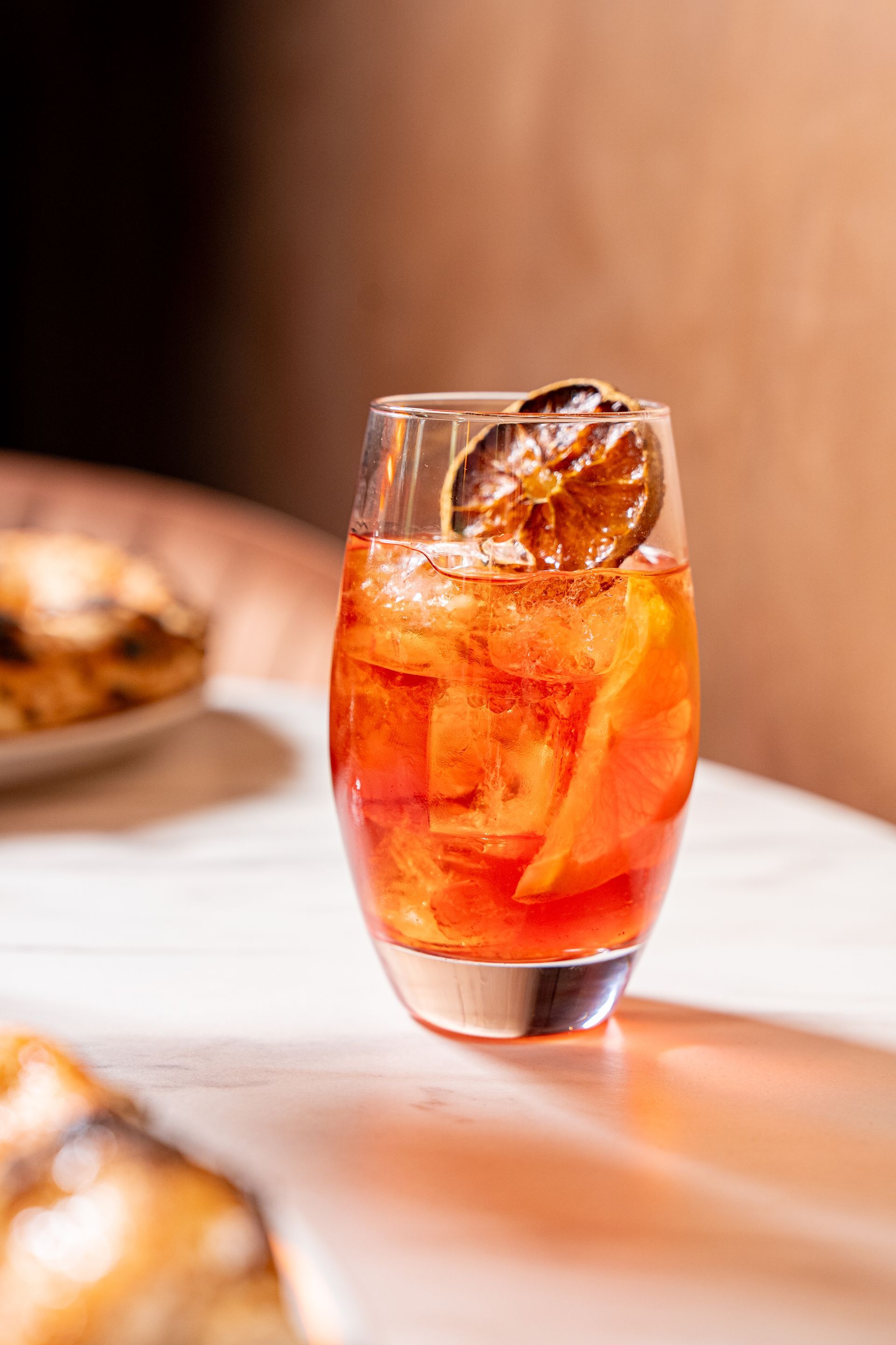 Eine Hand hält einen roten Cocktail mit Eis und einer Orangenscheibe auf einem kleinen Tablett.