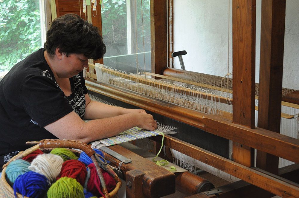 Eine Frau arbeitet an einem Webstuhl neben einem Korb mit Garn.