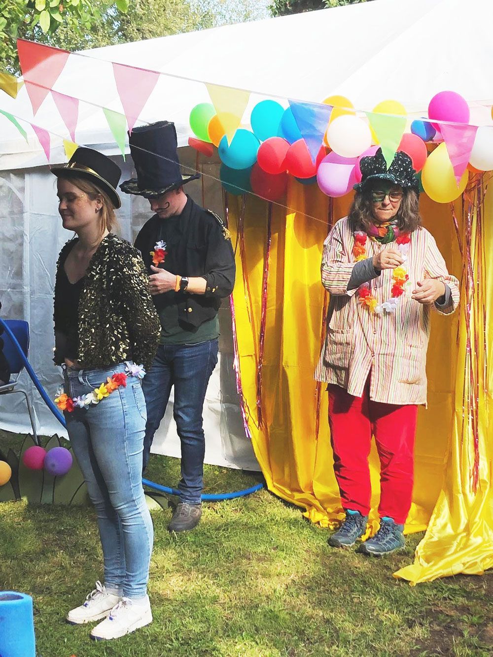 Drei Personen stehen vor einem mit Luftballons geschmückten Zelt.