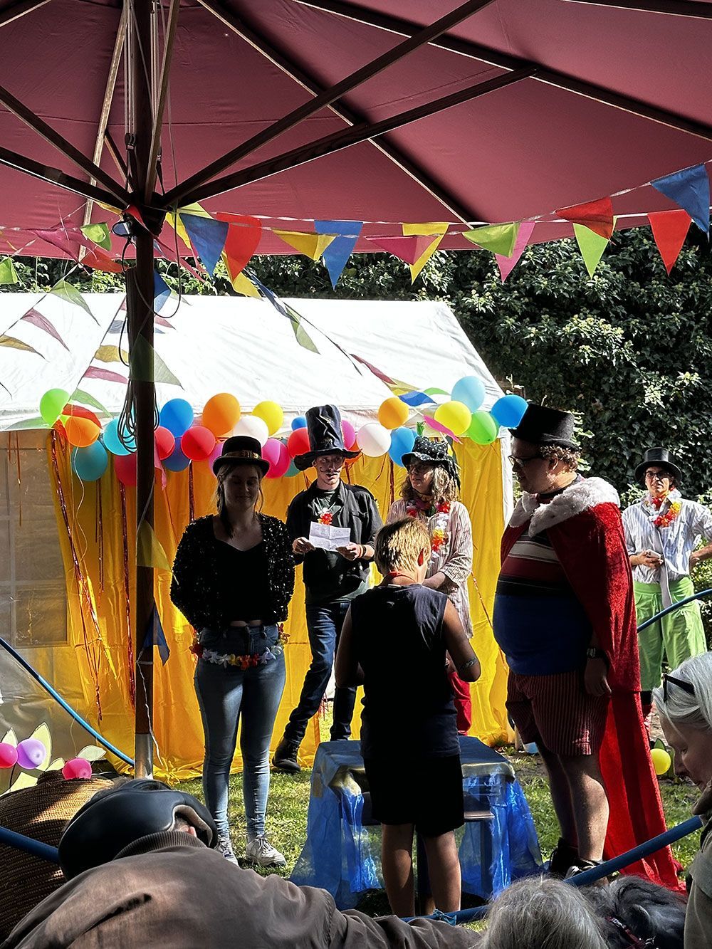 Eine Gruppe von Menschen steht auf einem Jahrmarkt unter einem Regenschirm.