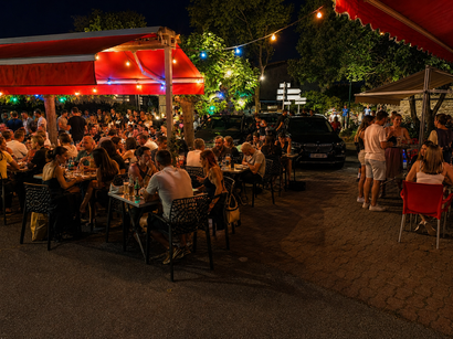 Terrasse extérieure avec des guirlandes lumineuses et des gens assis à des tables.