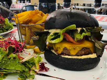 Cheeseburger au pain noir avec laitue et fromage, accompagné de frites et de salade sur une assiette blanche.