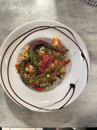 Salade gourmande dans un bol blanc, garnie d'herbes et de légumes, arrosée d'une sauce brune, sur une table grise.