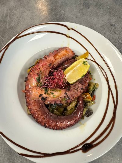 Assiette de fruits de mer avec quartier de citron, salade verte et filet de vinaigre balsamique sur une assiette blanche.