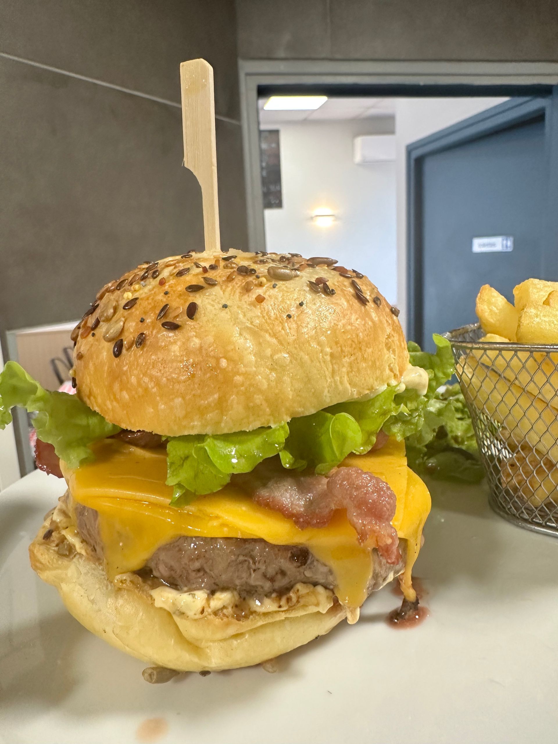 Un cheeseburger avec de la laitue et du fromage fondu est posé sur une table, accompagné de frites dans un panier métallique à proximité.