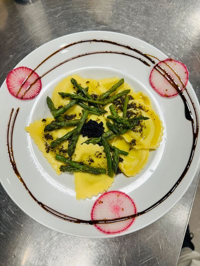 Pâtes jaunes dressées sur un plat blanc, garnies d'herbes vertes et de tranches de radis.