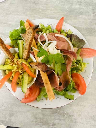 Salade composée avec laitue, tomate, concombre, gressins et prosciutto roulé sur une assiette blanche.