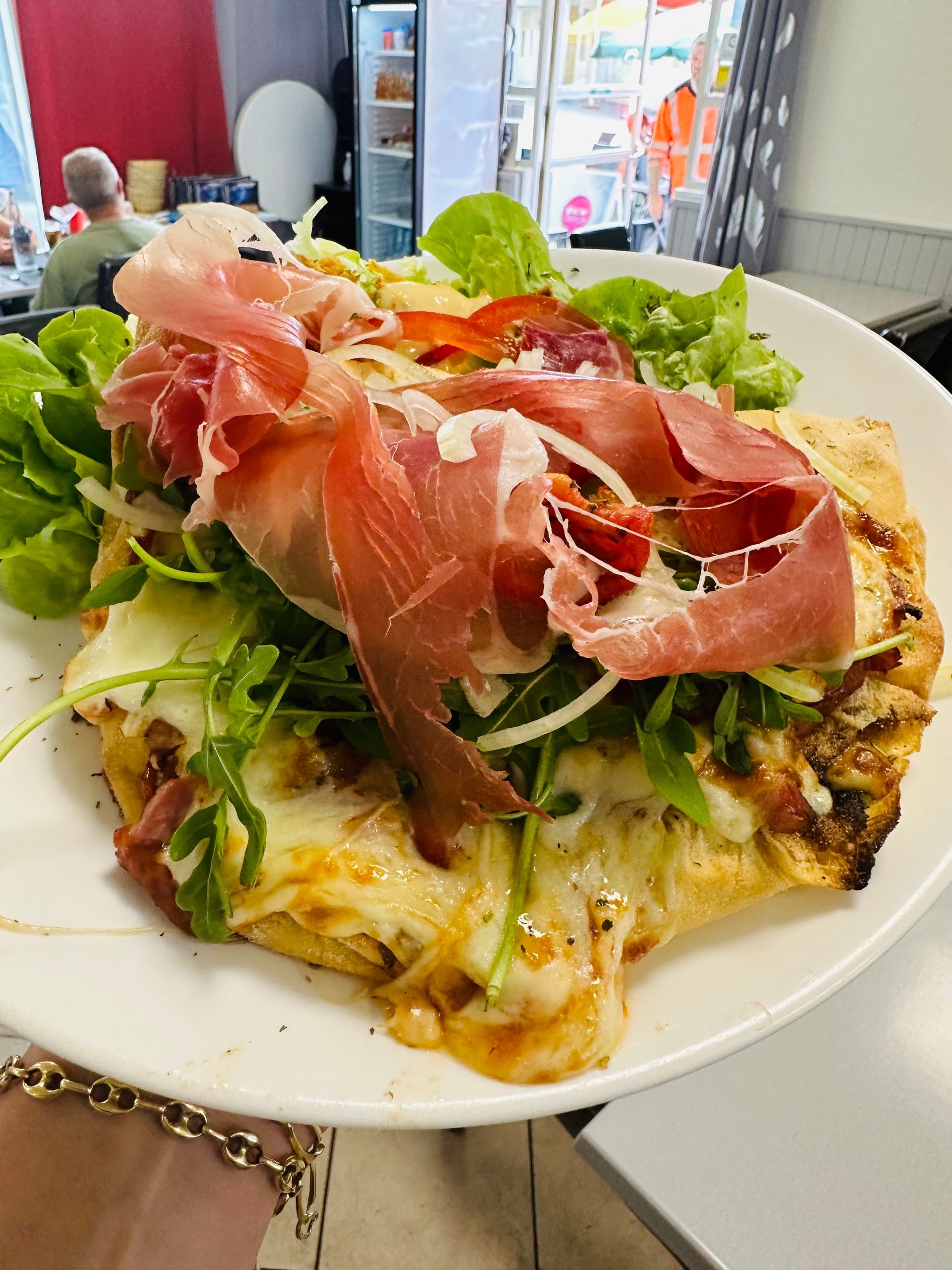 Tartine ouverte au prosciutto, à la salade et au fromage fondu, servie sur une assiette blanche.