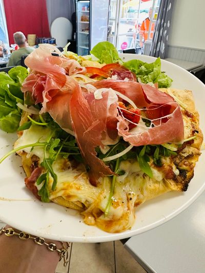 Omelette ouverte garnie de prosciutto, de légumes verts et de fromage, servie sur une assiette blanche.