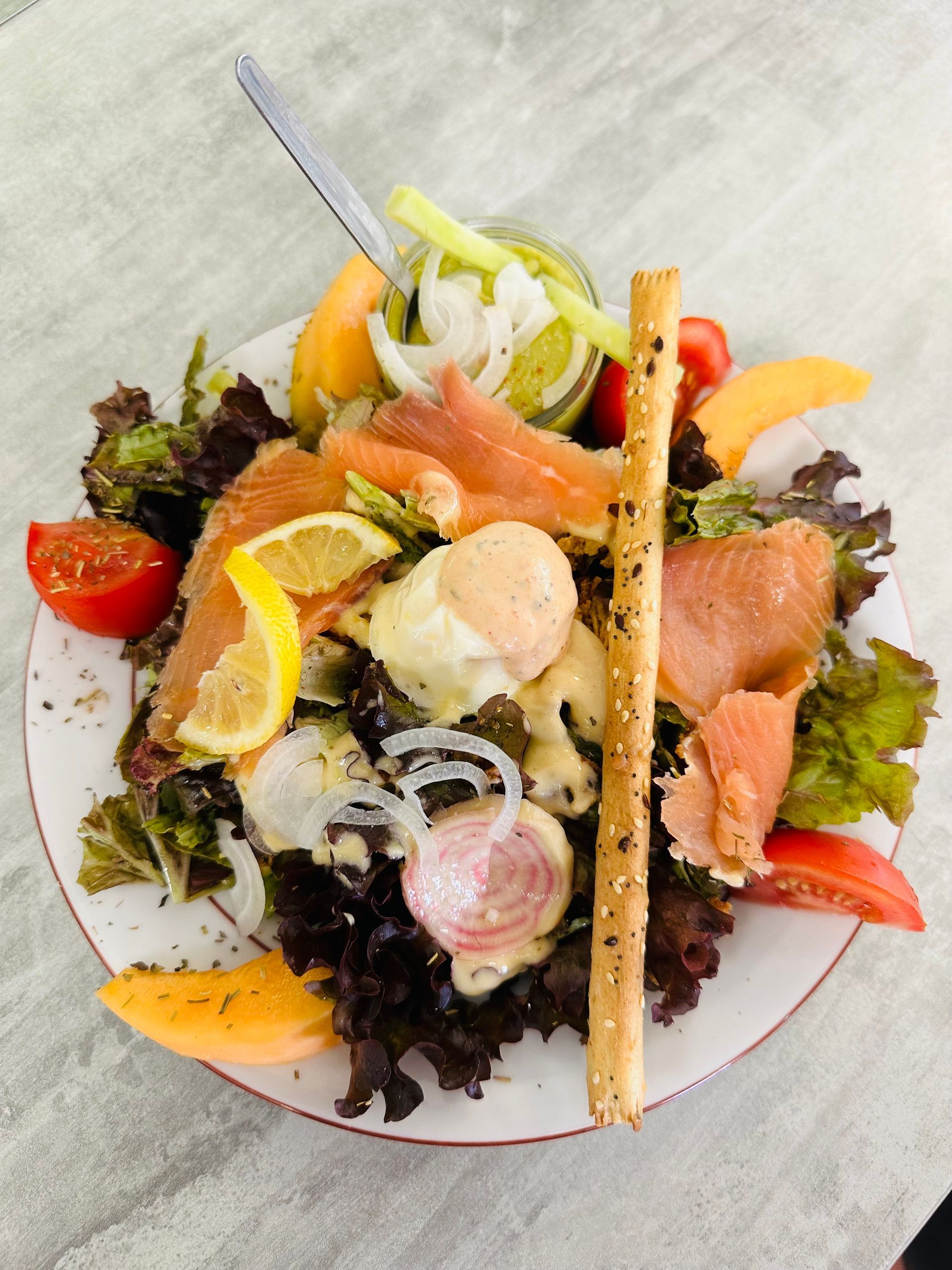 Assiette de salade avec saumon fumé, tranches d'agrumes, croûtons et mesclun sur une table.
