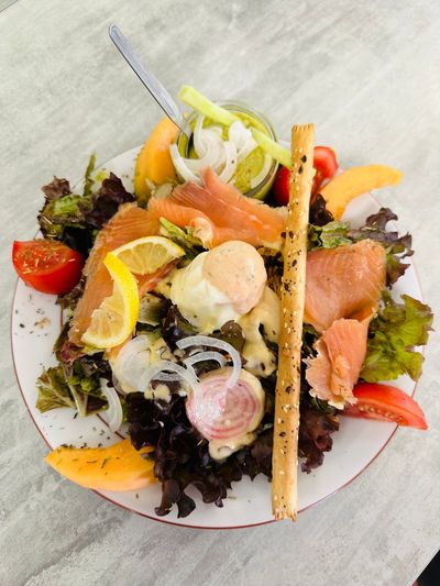 Salade composée avec saumon, tranches d'agrumes, tomates cerises et gressins sur une assiette blanche.