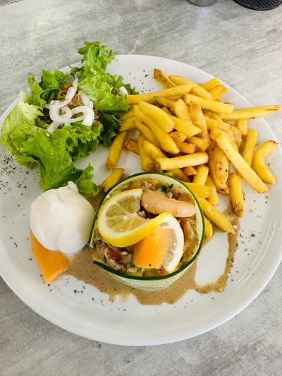 Salade avec citron et œuf poché, frites et salade verte sur une assiette blanche.