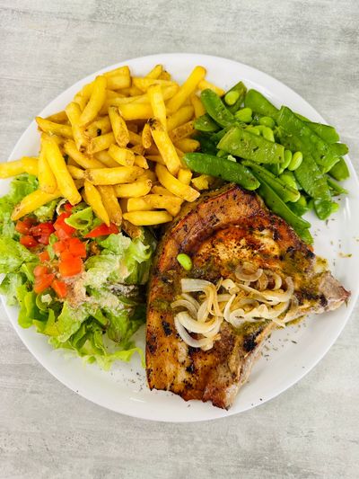 Assiette de poulet assaisonné avec frites, haricots verts et salade sur une assiette blanche.