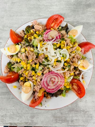 Salade composée de thon, de maïs, d'œufs durs, de rondelles d'oignon et de quartiers de tomate, servie dans une assiette blanche.