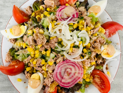 Salade colorée avec thon, maïs, rondelles d'oignon, œufs, tomates et verdure sur une assiette blanche.
