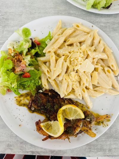 Assiette de pâtes avec salade et poisson grillé, garnie de tranches de citron, servie dans un plat blanc.