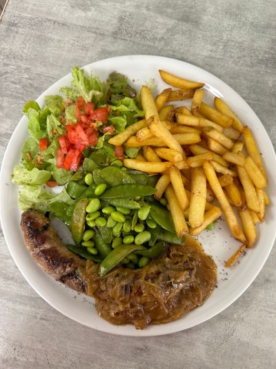 Assiette avec steak, frites, haricots verts, petits pois et salade sur une table.