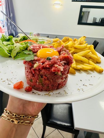 Assiette de tartare garnie de jaune d'œuf, frites et salade.