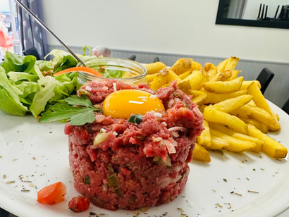 Steak tartare avec jaune d'œuf, frites et salade sur une assiette blanche.