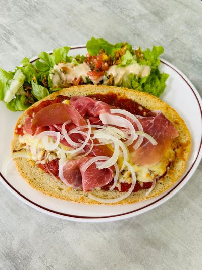Crêpe salée garnie de jambon et d'oignons, servie avec une salade verte sur une nappe blanche.