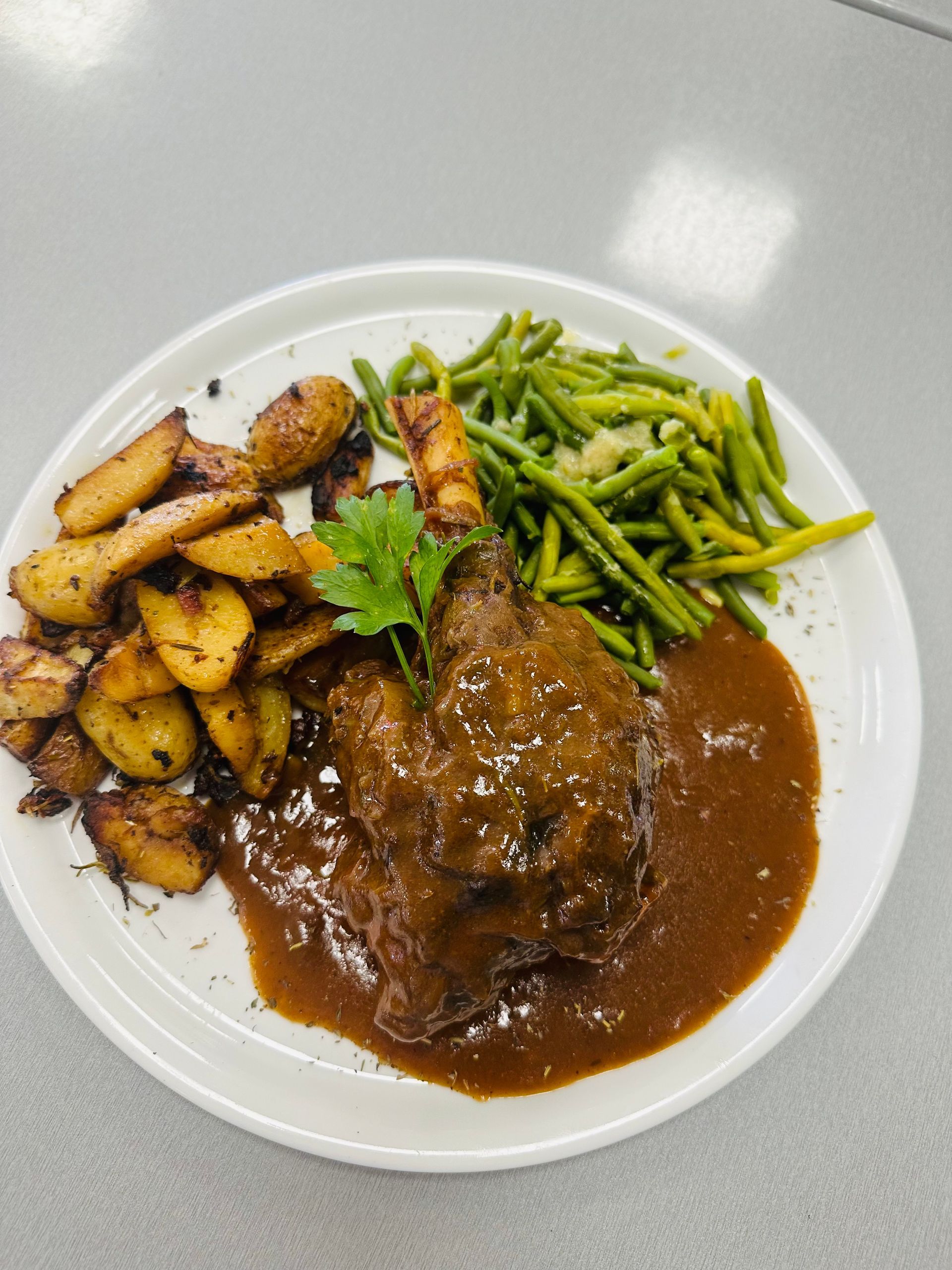 Viande servie dans une assiette blanche, nappé de sauce brune et accompagné de pommes de terre rôties et de haricots verts.
