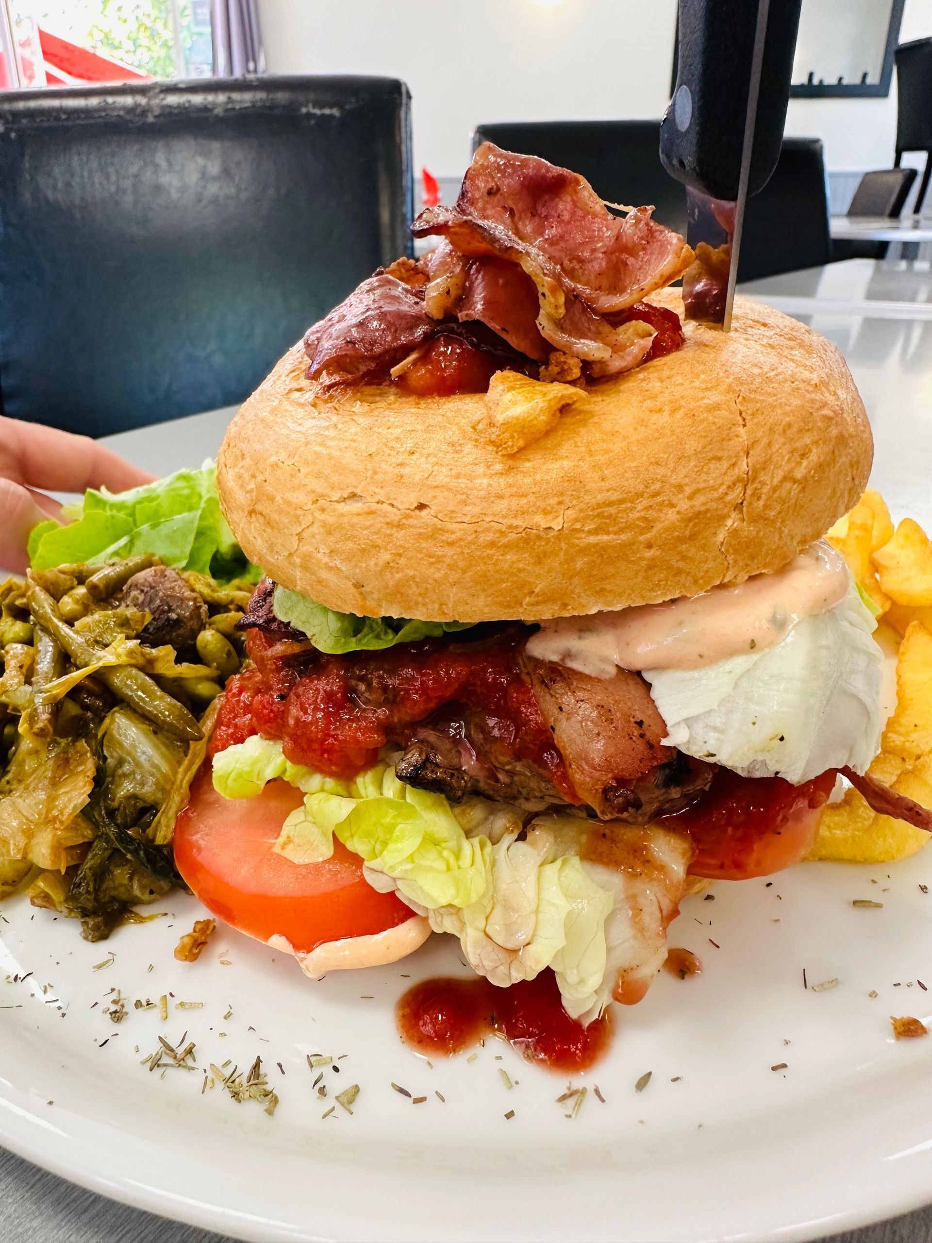 Burger gourmet servi dans une assiette avec bacon, laitue, tomate, sauce et cornichons.