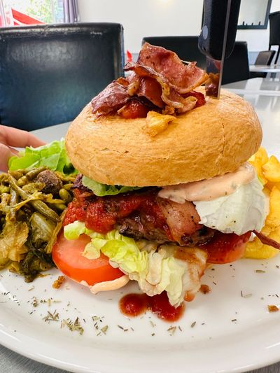 Burger garni de bacon, de laitue, de tomate et de sauce, servi sur une assiette blanche, accompagné de légumes verts.
