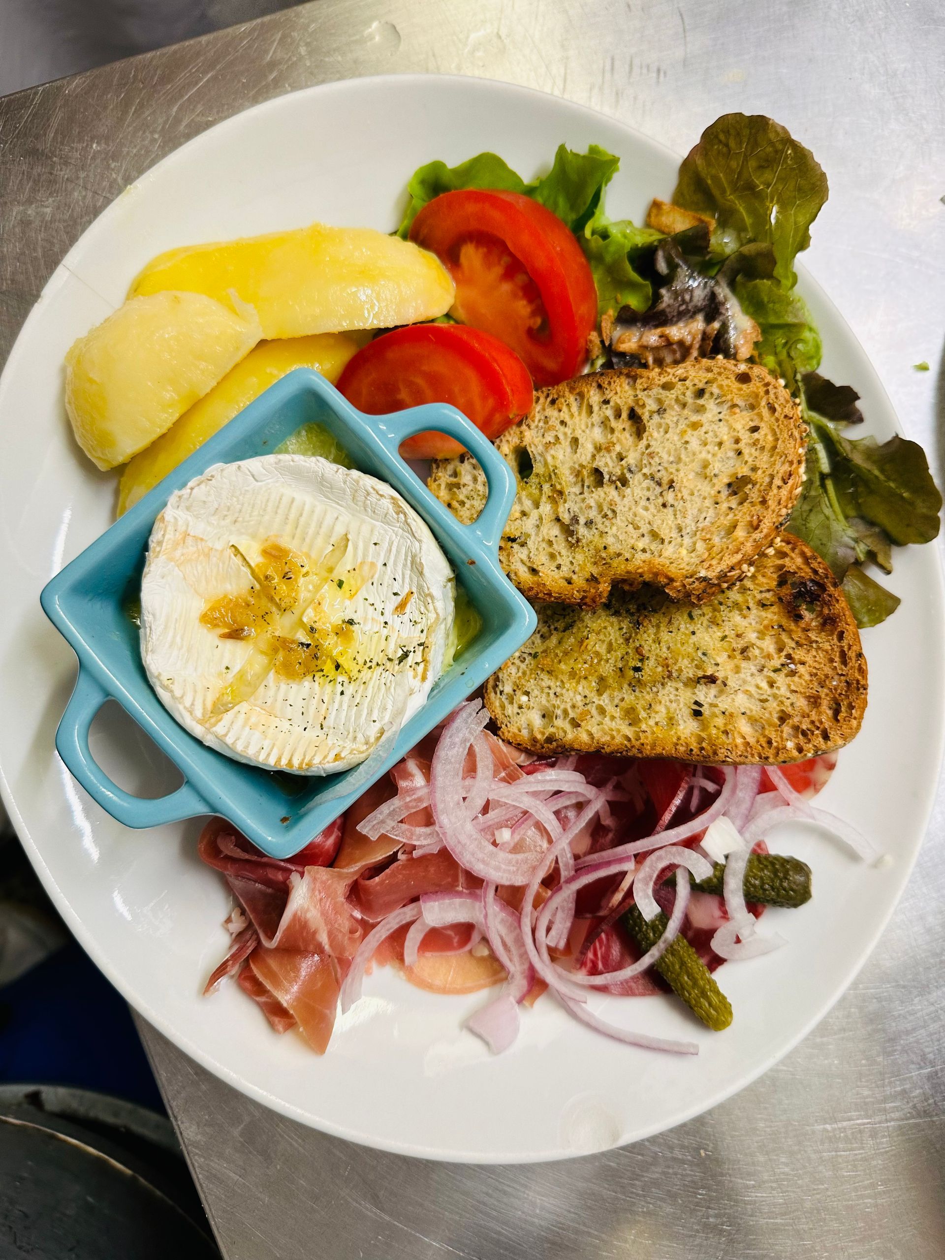 Repas servi à l'assiette avec du pain grillé, oignons rouges, tomate, laitue, citron et un petit bol de fromage rôti aux herbes.