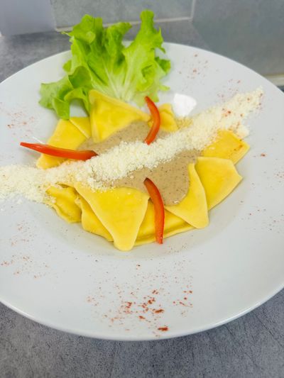 Triangles de pâtes avec du fromage râpé et des tranches de poivron rouge sur une assiette blanche, garnis de laitue.