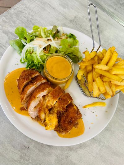 Poulet servi avec sauce, frites et salade sur une table blanche.