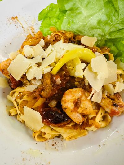 Pâtes aux crevettes avec du fromage râpé et une feuille de laitue verte sur une assiette blanche.