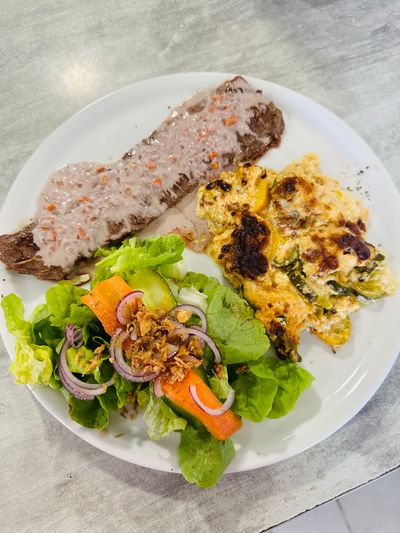 Assiette composée d'un filet de viande grillé, d'œufs brouillés au fromage et d'une salade verte avec des carottes et des oignons rouges.