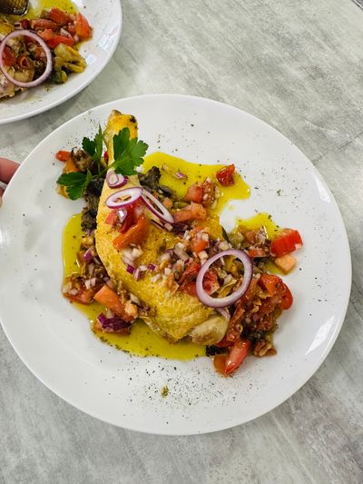 Assiette de poisson garnie d'oignons rouges et d'herbes aromatiques, servie avec des légumes colorés sur une table légère.